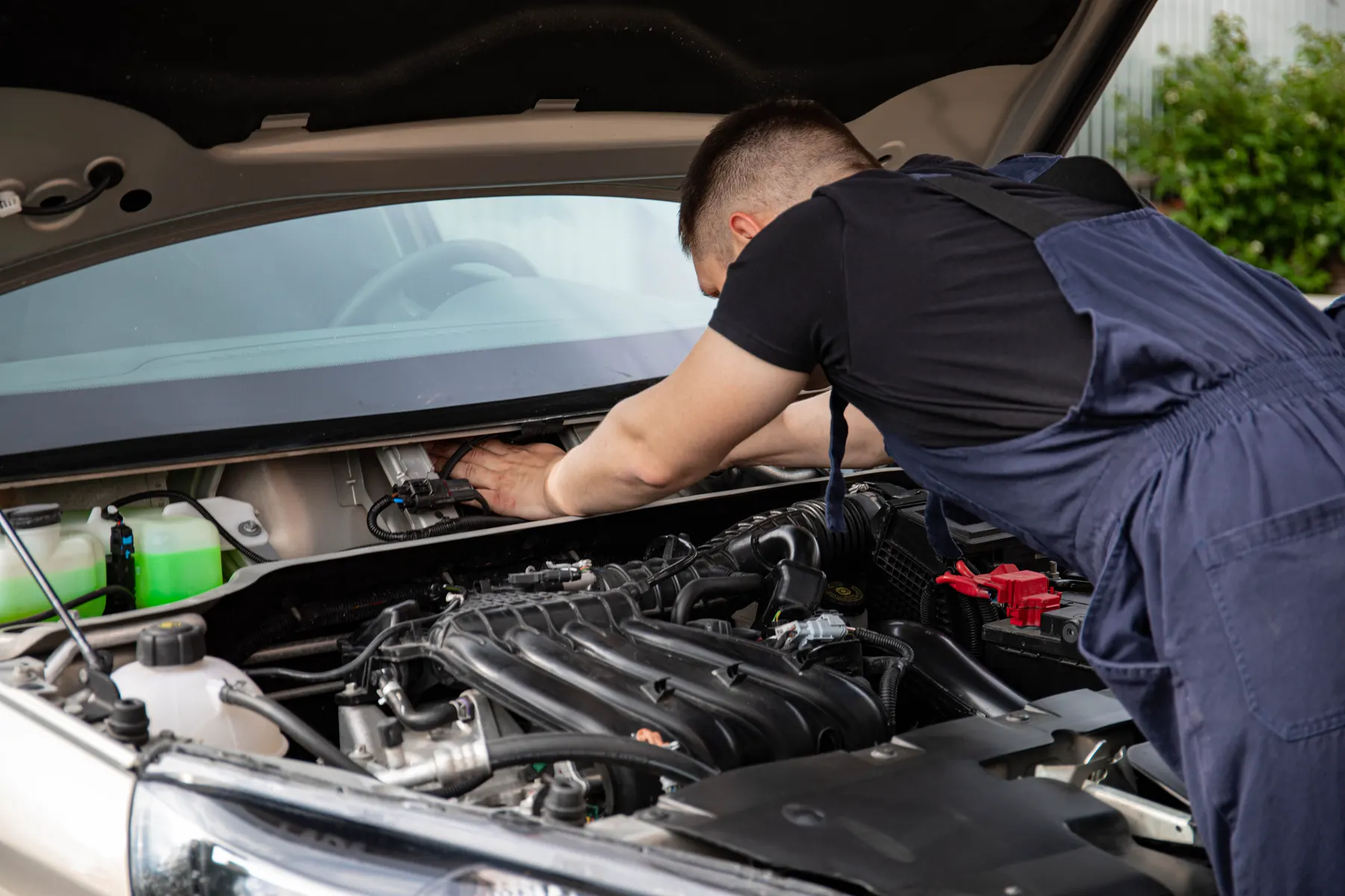 Mechanic in overalls leaning into an engine bay